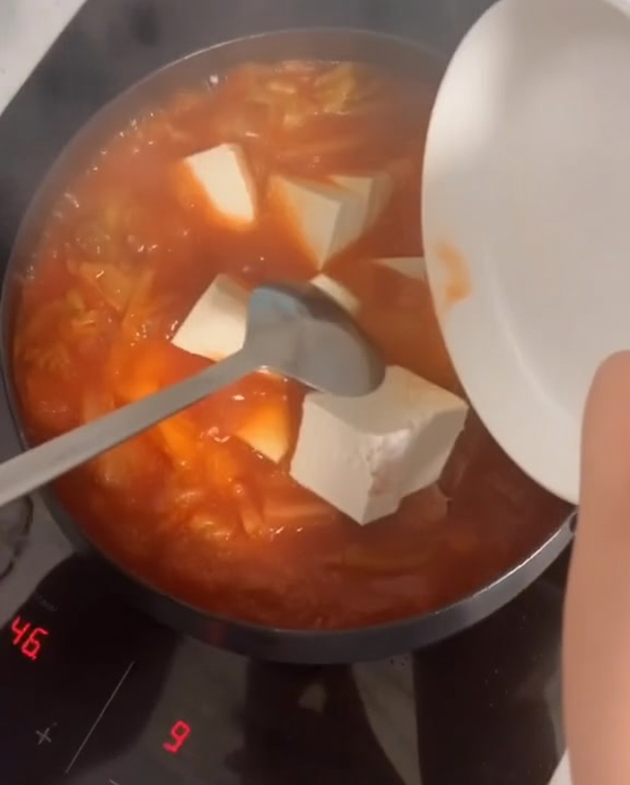 Kostki miękkiego tofu dodawane do bulgoczącego, czerwonego gulaszu kimchi.