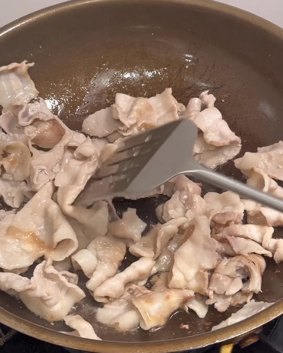 Cebula, szczypiorek i plasterki chili wrzucane na patelnię do boczku.