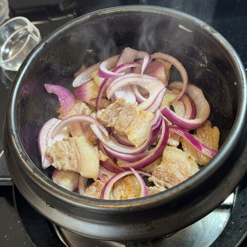 Kimchi wymieszane z boczkiem i cebulą w kamiennym garnku.