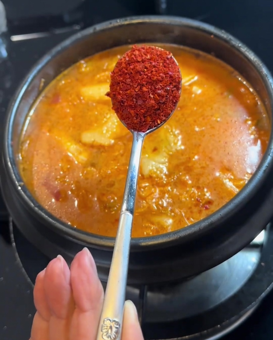 Płatki chili dodawane do gulaszu za pomocą łyżki.