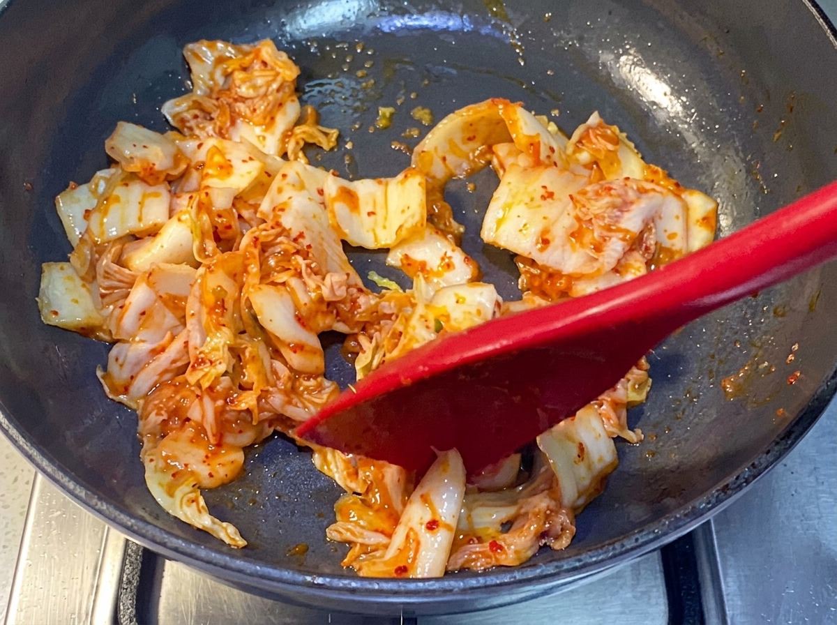 Kimchi smażone na patelni za pomocą czerwonej silikonowej szpatułki.