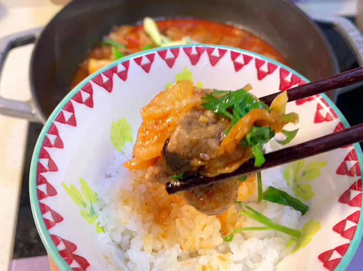 Zbliżenie na łyżkę mieszającą czerwoną koreańską pastę chili w bulgoczącym gulaszu z kimchi i żeberkami.
