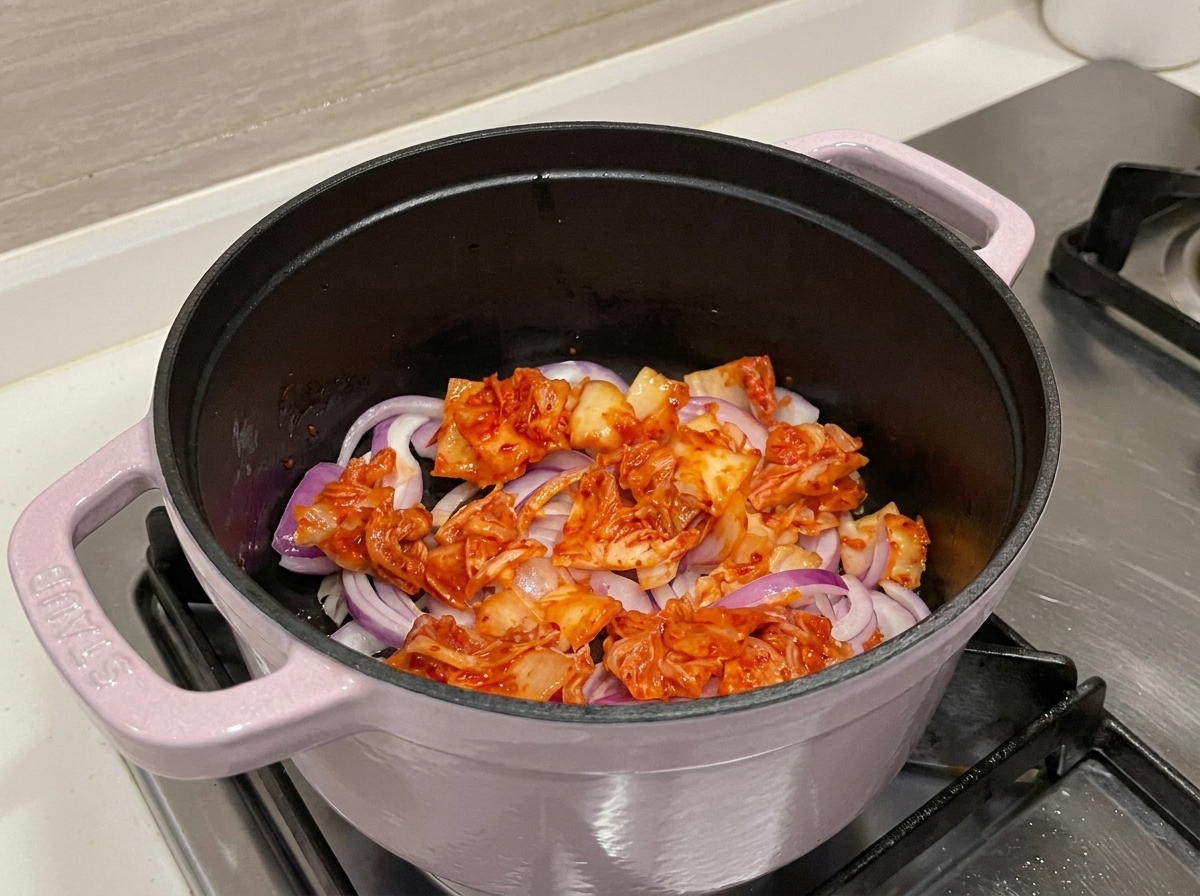 Zbliżenie na jaskrawoczerwone kimchi i cebulę smażone w garnku, uwalniające aromatyczne soki.