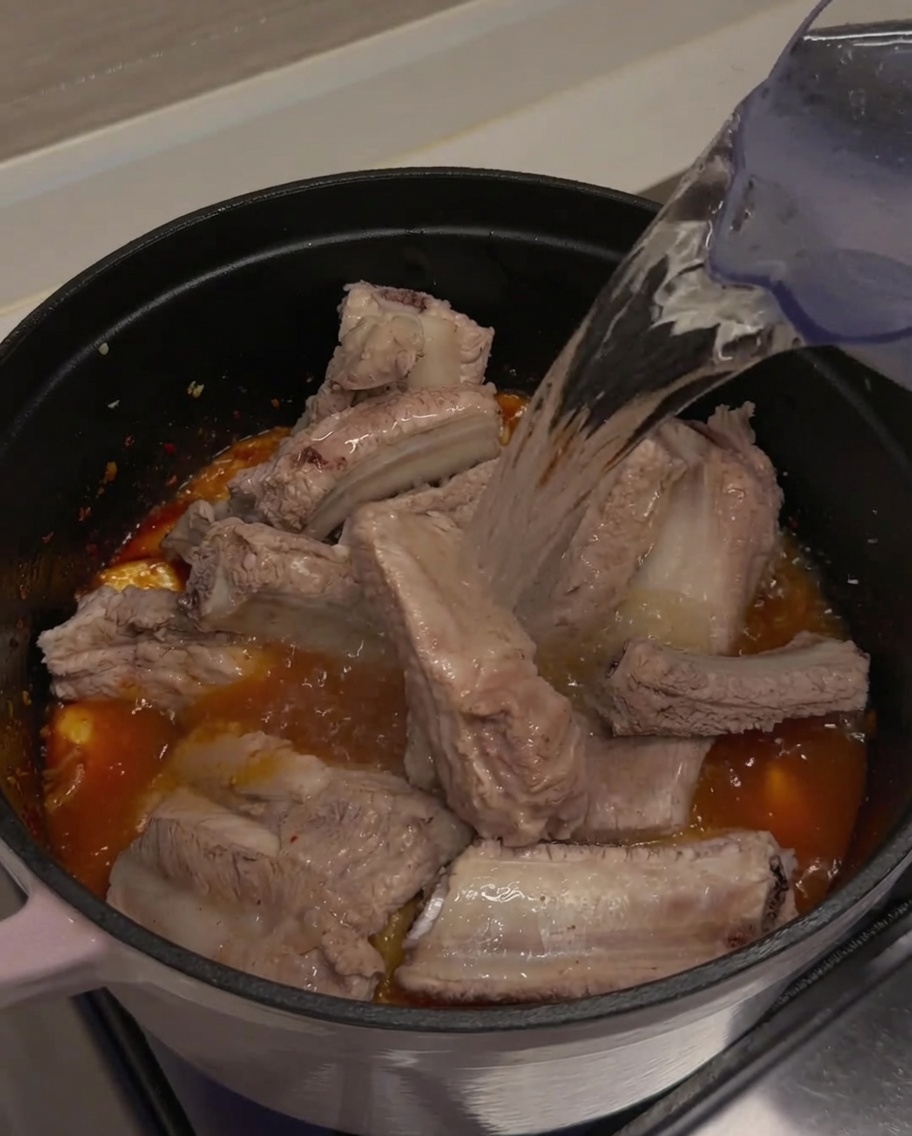 Czysta woda nalewana z dzbanka do garnka, całkowicie zakrywająca żeberka i kimchi.