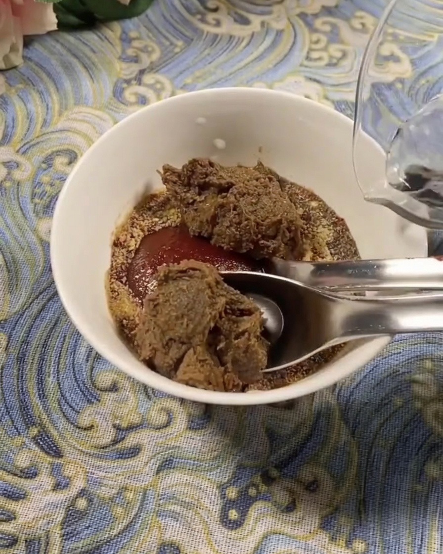 Zbliżenie na białą miseczkę zawierającą mieszankę koreańskiej pasty chili i pasty sojowej, do której wlewana jest świeża woda.