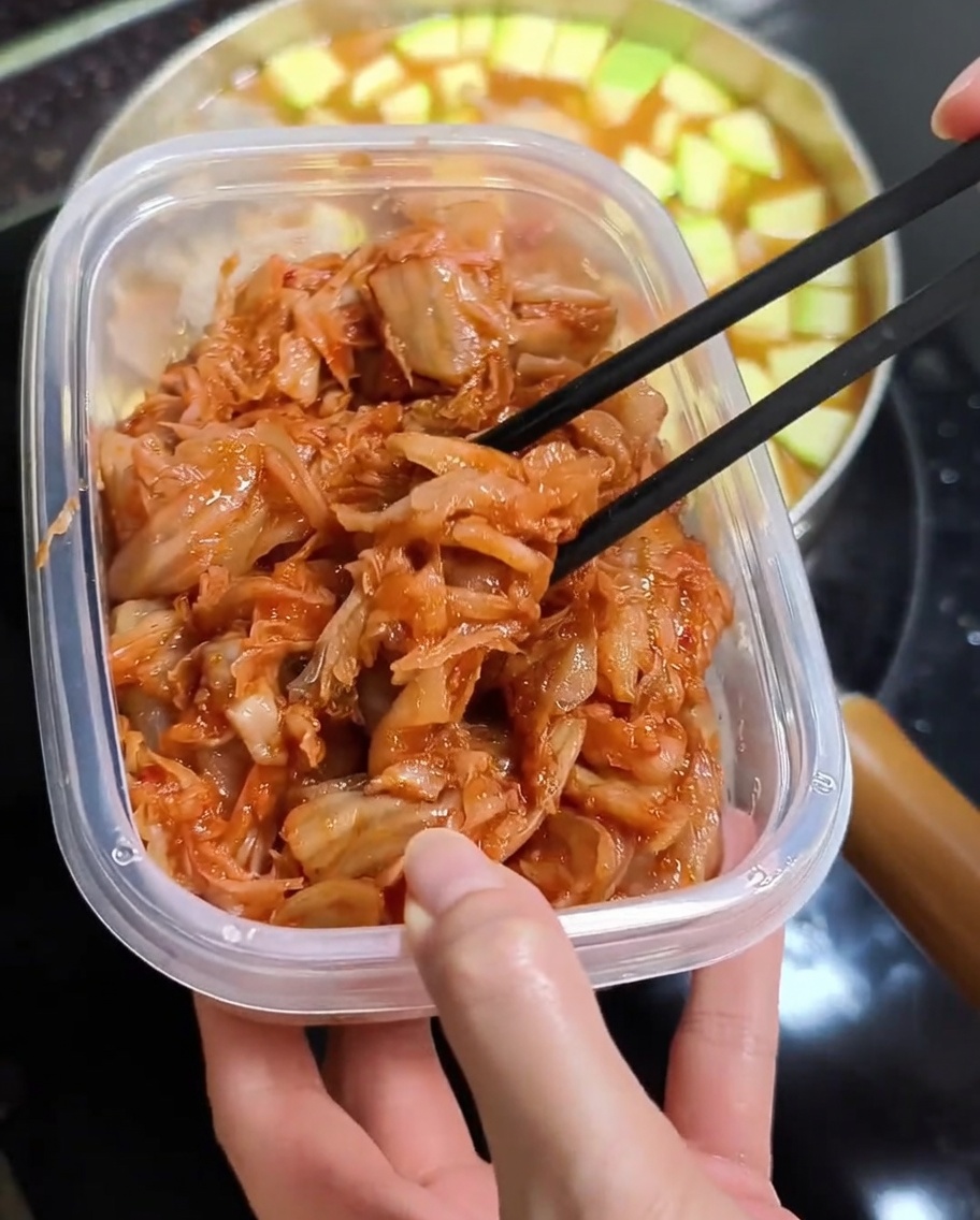 Pałeczki przenoszące jasnoczerwone posiekane kimchi do garnka z gorącym gulaszem.