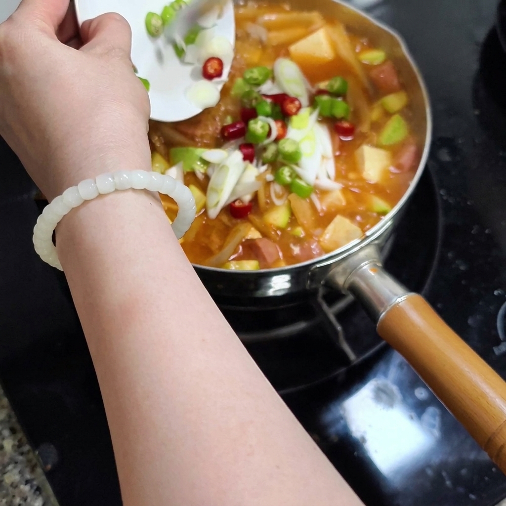 Dłoń trzymająca mały talerz, zsuwająca chili i szczypiorek do garnka.