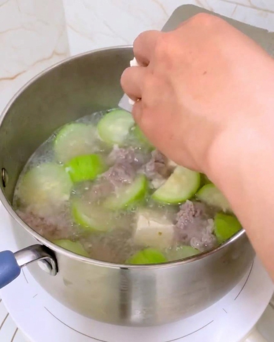 Dłoń wrzucająca kostki białego tofu do garnka z zupą.