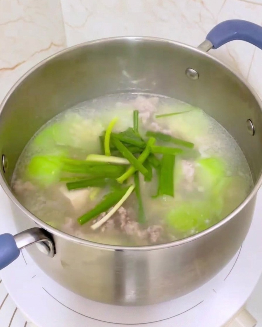 Garnek z zupą z trukwą, tofu i mięsem doprawiany szczypiorkiem i mieszany chochlą.