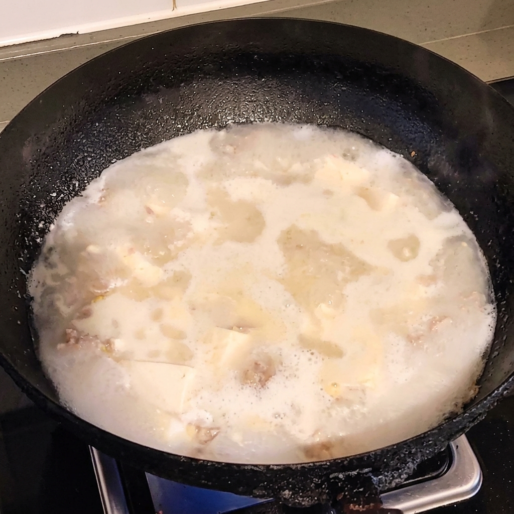 Pokrojone w kostkę białe tofu dodawane do garnka z wrzącym bulionem wieprzowym.
