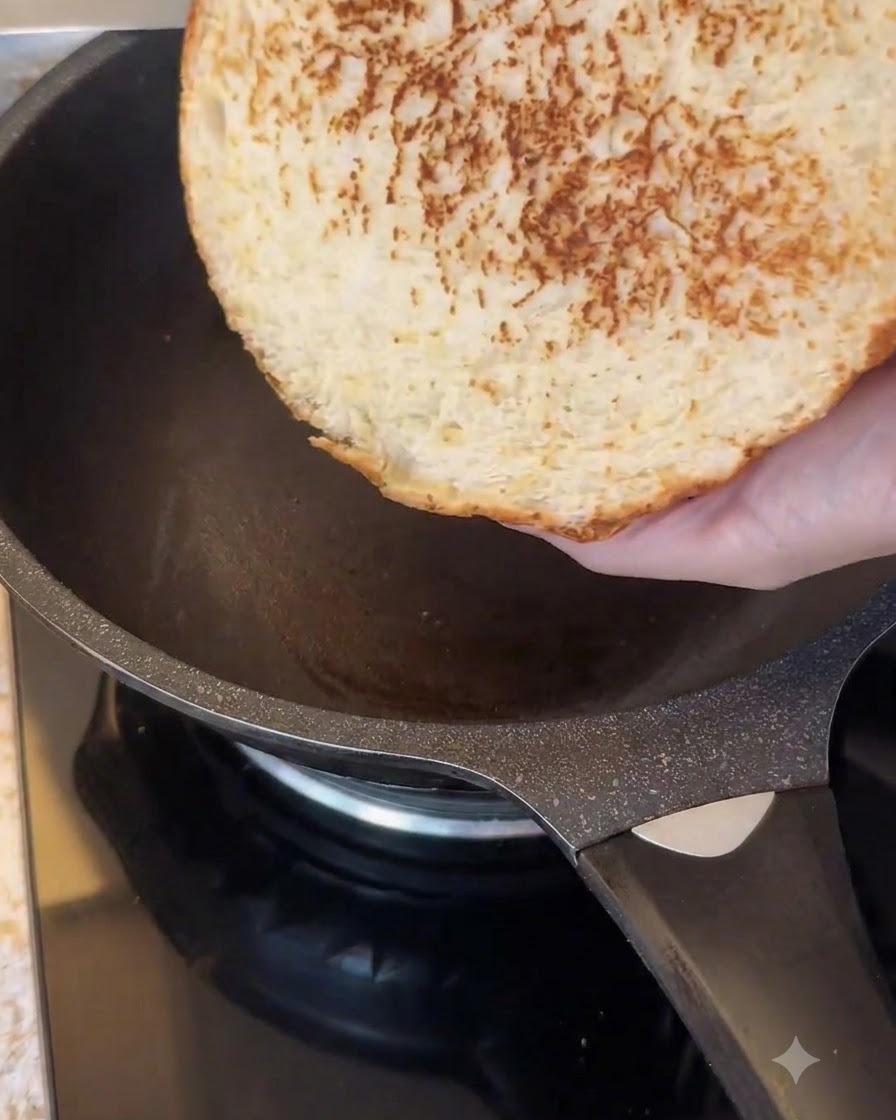 Przekrojona strona dużej bułki do burgera podpiekana na ciemnej patelni nieprzywierającej.