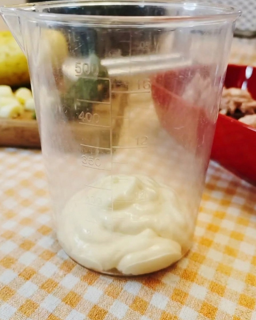 Kopka gęstego majonezu spoczywająca na dnie przezroczystego kubka z podziałką.
