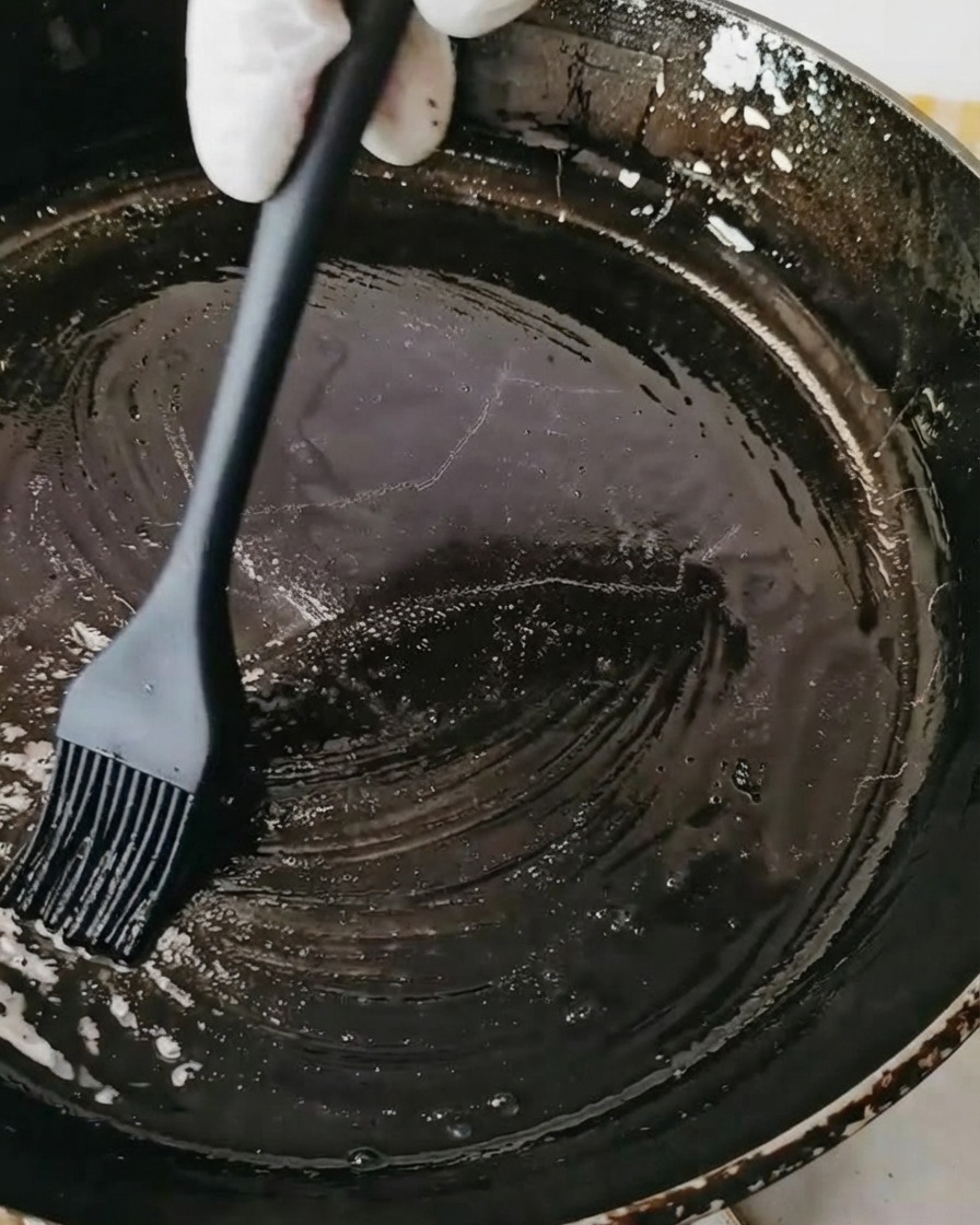 Czarna patelnia smarowana olejem za pomocą czarnego silikonowego pędzelka cukierniczego.