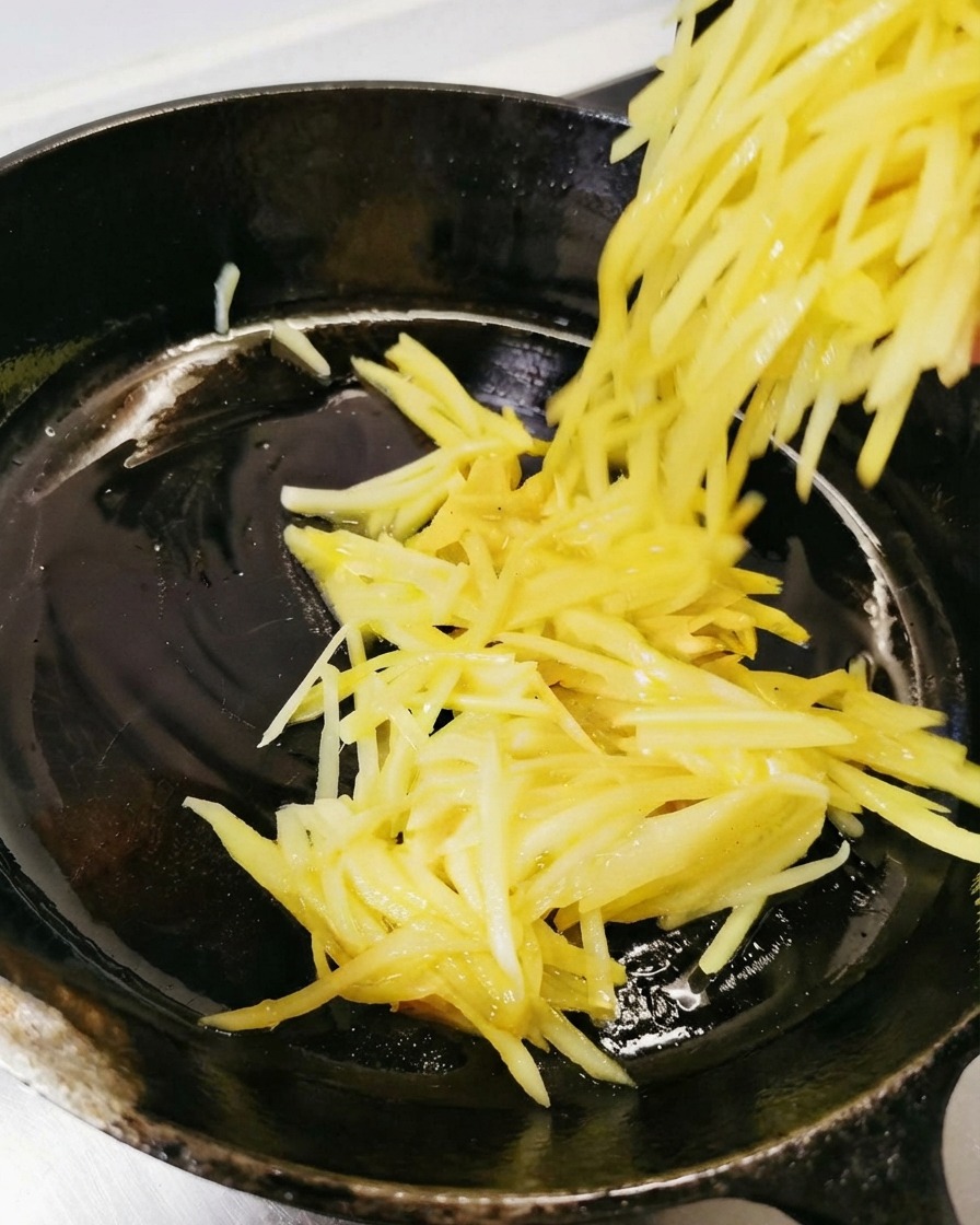 Starte ziemniaki przekładane i rozprowadzane na naoliwionej czarnej patelni.