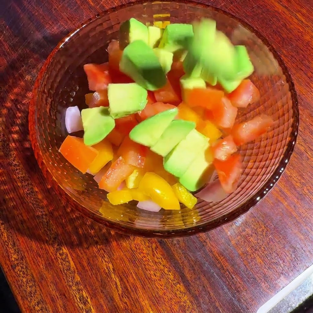 Pokrojone warzywa i awokado w szklanej misce mieszane razem z sosem.