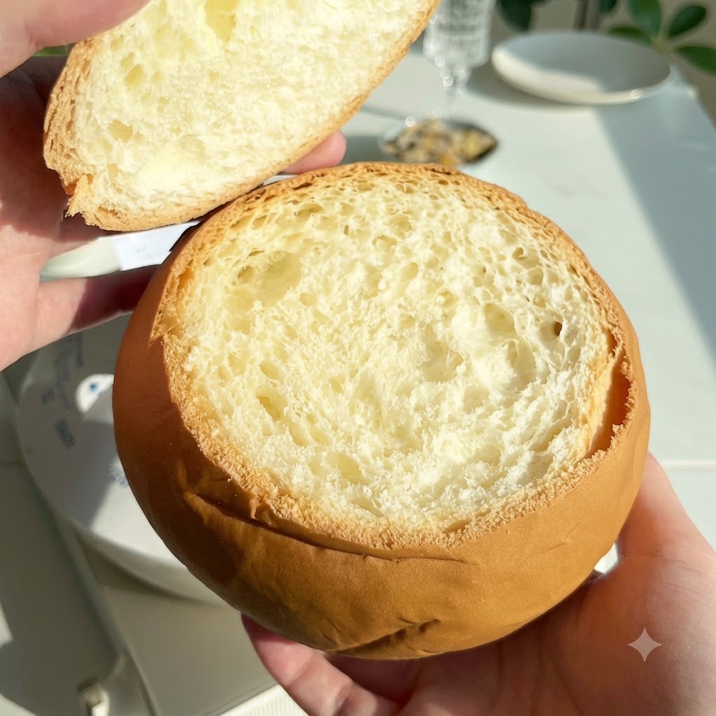 Okrągły, wydrążony bochenek chleba trzymany z odciętą górną pokrywką obok.