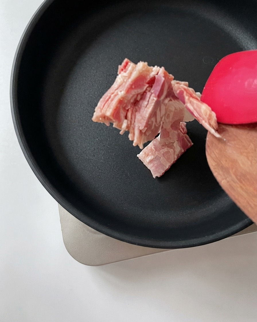 Posiekany boczek przekładany za pomocą drewnianej łopatki na gorącą, czarną patelnię.