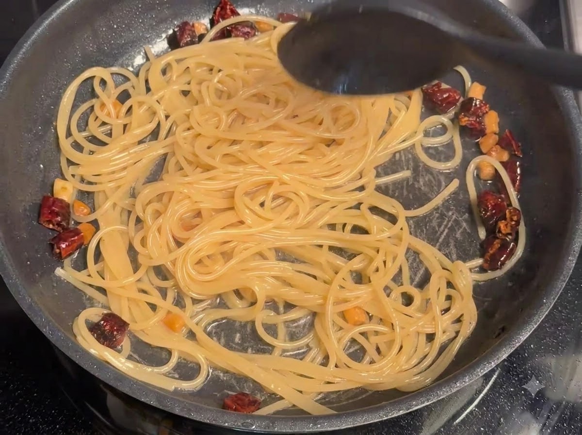 Woda z gotowania makaronu mieszana na patelni ze spaghetti i kawałkami wieprzowiny.