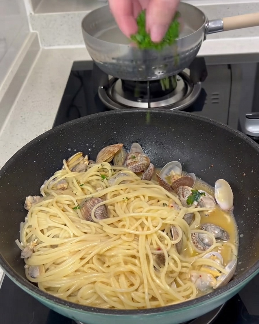 Świeżo posiekana zielona pietruszka posypywana z góry na patelnię ugotowanego spaghetti i małży.