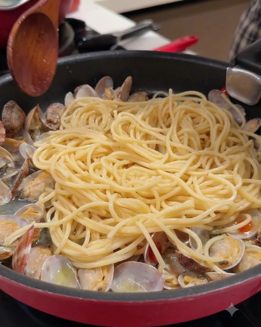 Drewniana łyżka i spaghetti w patelni z otwartymi małżami i bulionem.