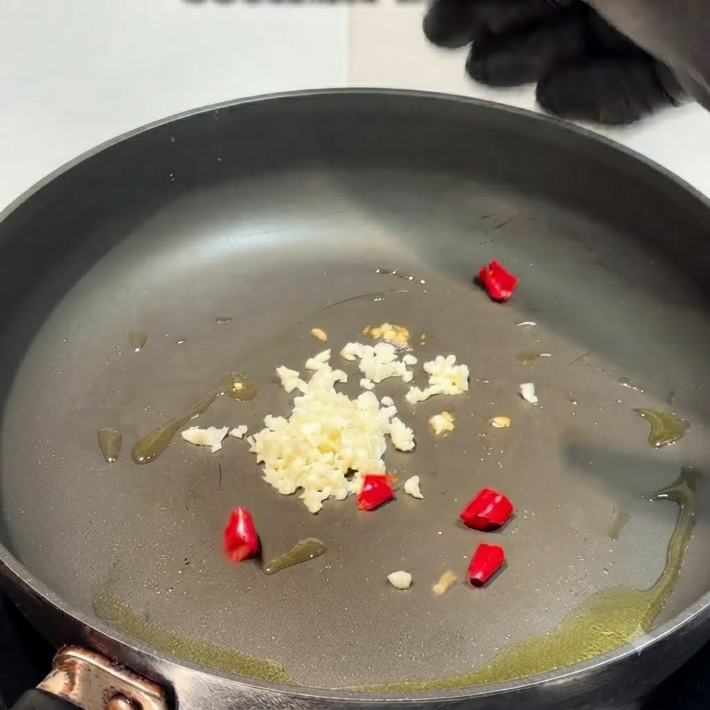Posiekany czosnek i czerwona papryczka chili smażące się na patelni z oliwą.