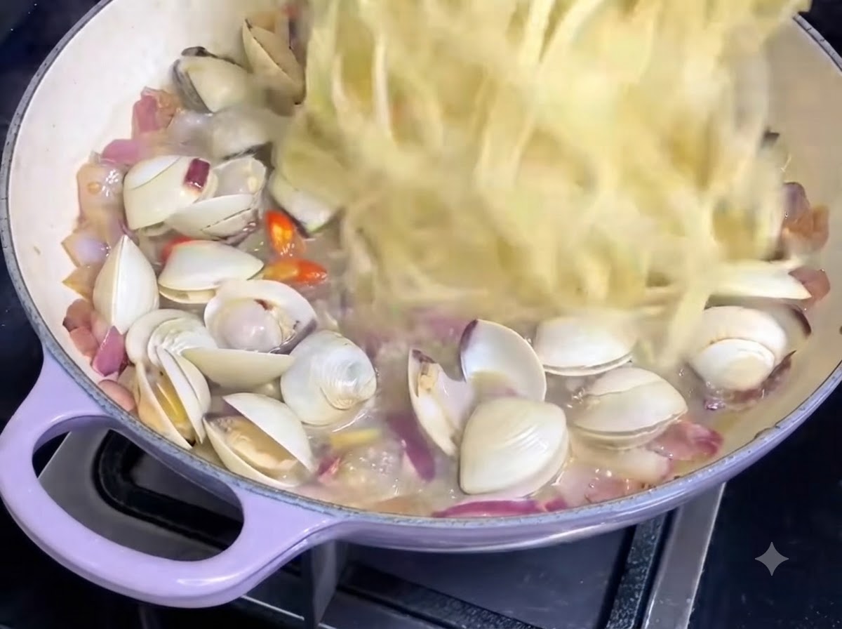 Ugotowane nitki spaghetti wrzucane na patelnię zawierającą sos z małży i cebulę.