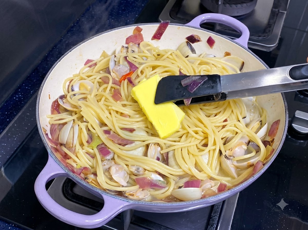 Kawałek żółtego masła topiący się na patelni z wymieszanym spaghetti i małżami.
