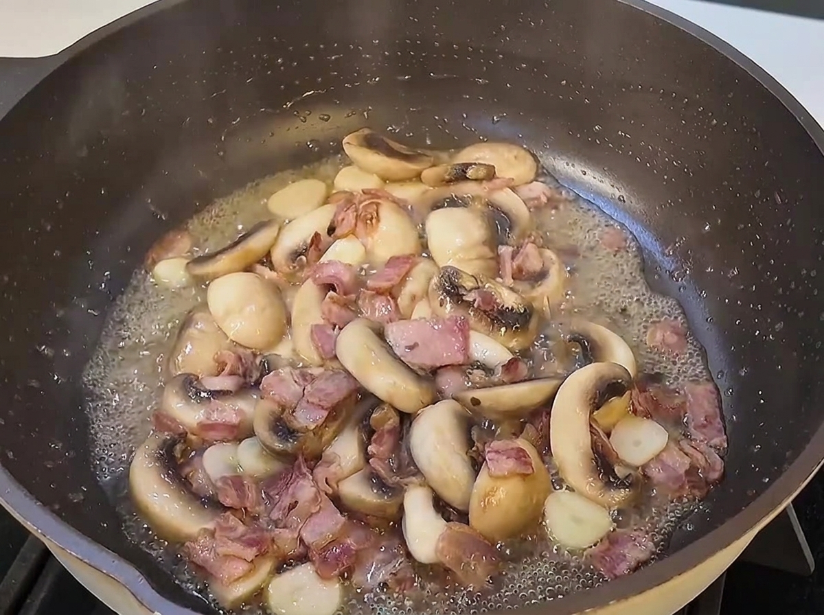Ugotowane nitki spaghetti wrzucane do dużej patelni z podsmażonymi grzybami i boczkiem.