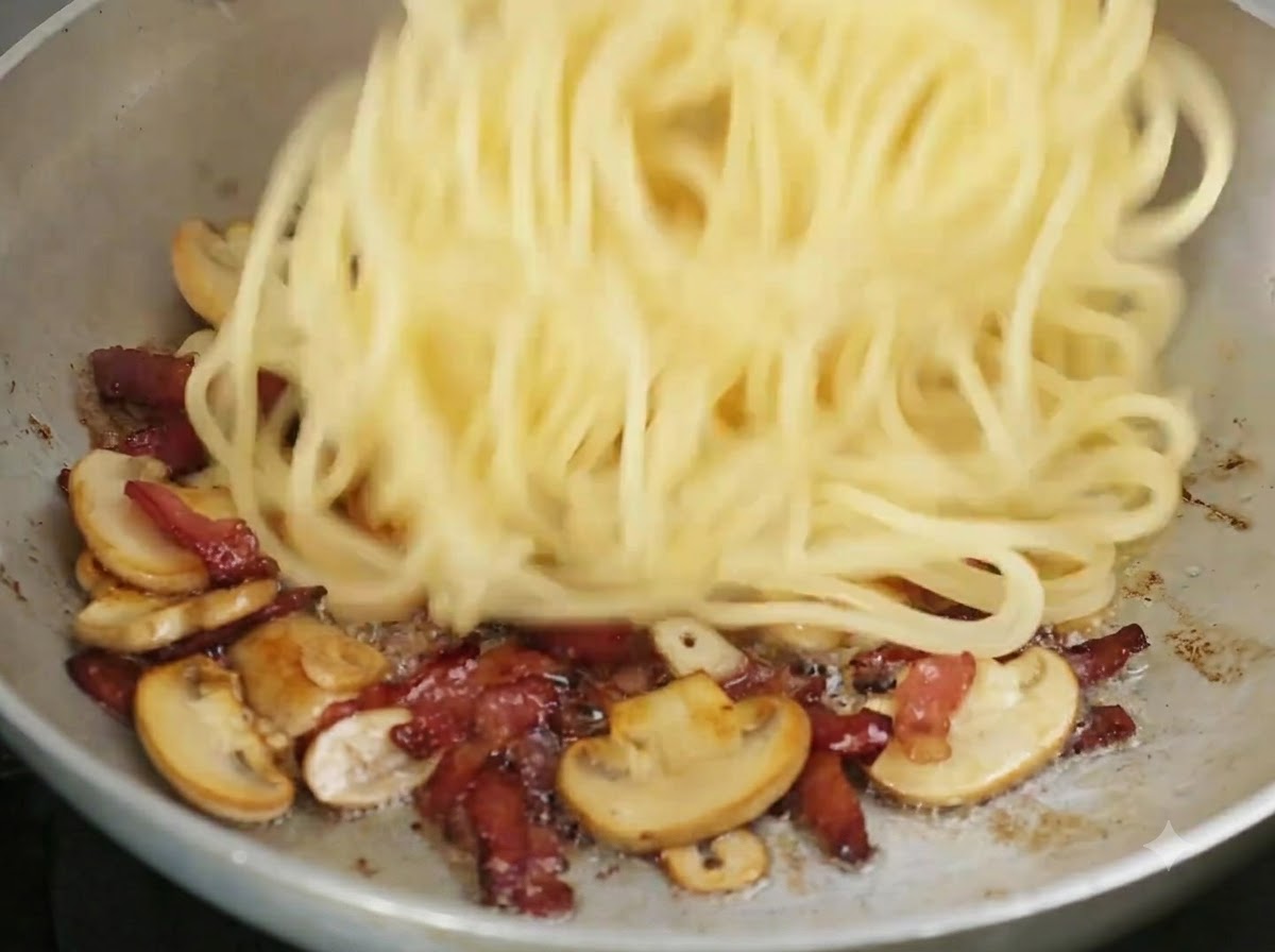Ugotowane spaghetti wrzucane na patelnię do podsmażonych składników.