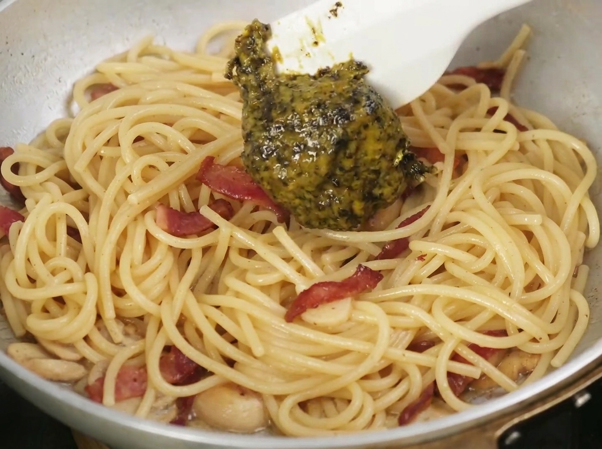 Pasta z czarnej trufli nakładana łyżką na patelnię z ugotowanym makaronem i boczkiem.
