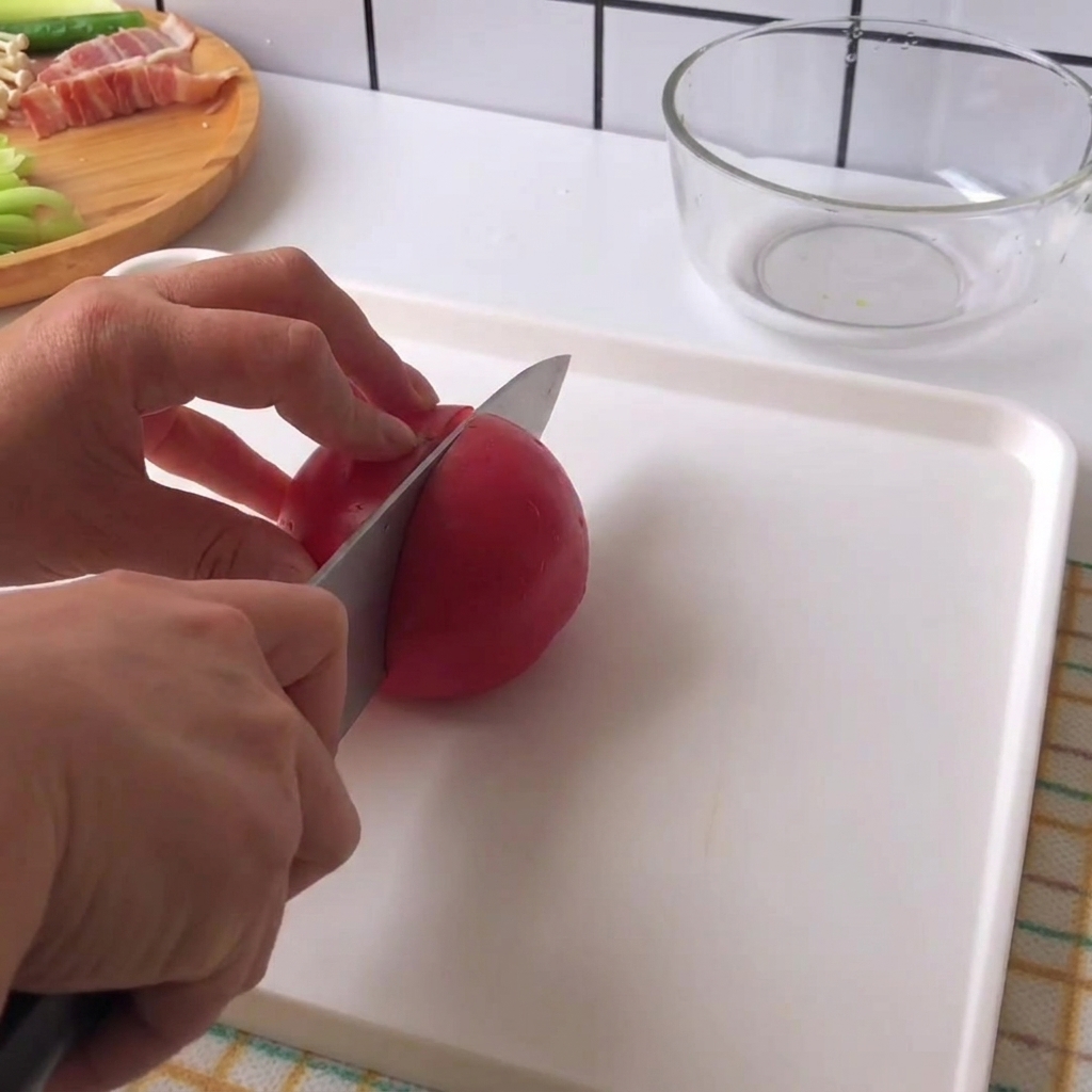 Ręce trzymające nóż krojący świeżego czerwonego pomidora na kawałki na białej desce do krojenia.