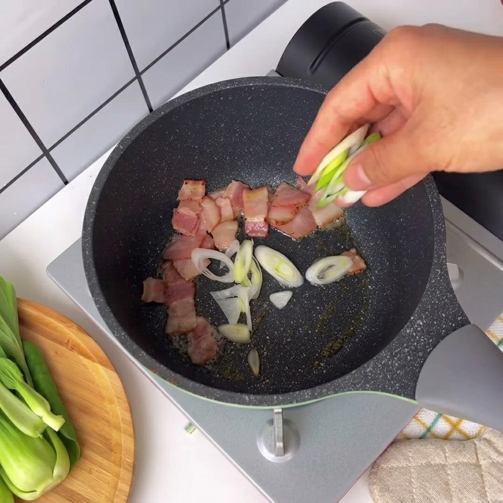 Posiekana zielona cebulka i papryczka chili posypywane na patelnię ze skwierczącymi kawałkami boczku.