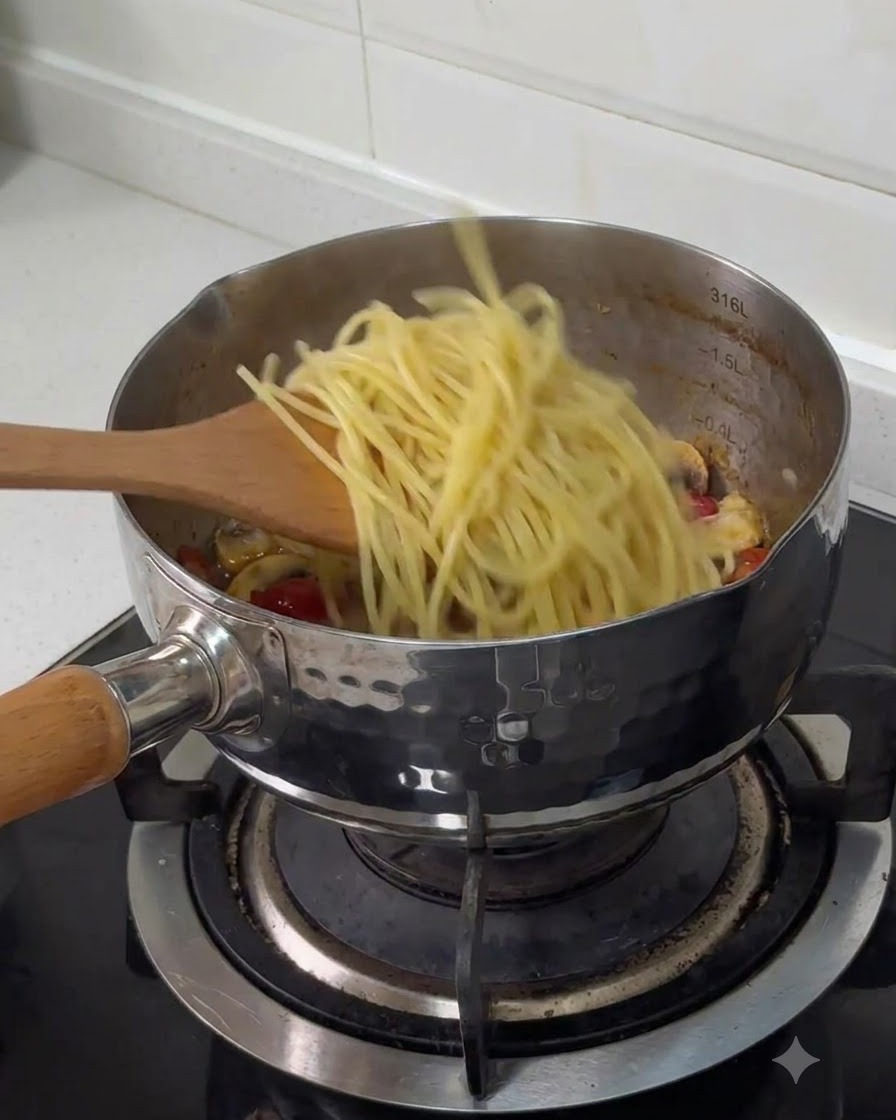 Ugotowane spaghetti przekładane łopatką do garnka ze stali nierdzewnej z pozostałymi składnikami.