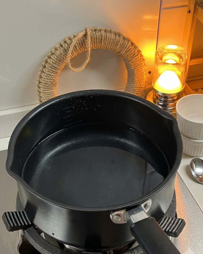 Suchy makaron fusilli wrzucany do garnka z wrzącą wodą na kuchence.