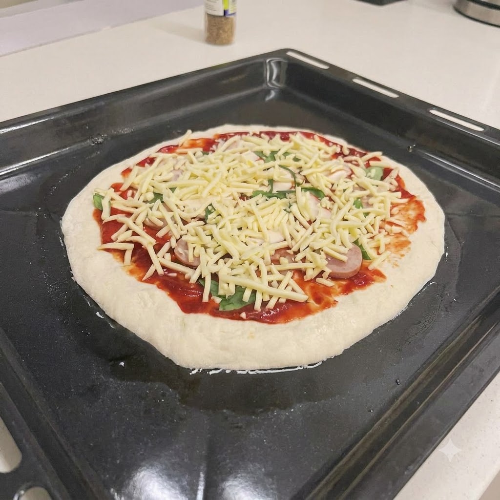 Surowa pizza z sosem, plastrami kiełbasy, świeżą bazylią i tartym serem na czarnej blasze do pieczenia.