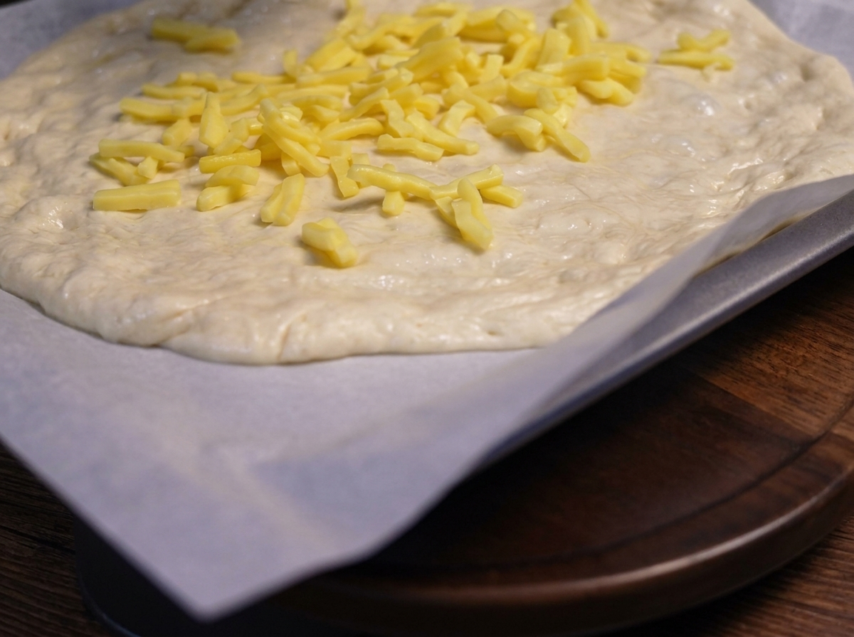 Podsmażone pokrojone grzyby ułożone na wierzchu warstwy sera na cieście do pizzy.