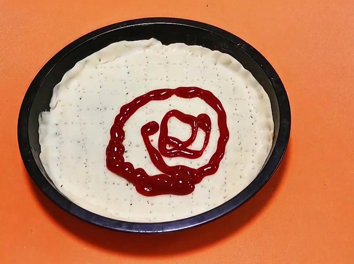 Wzorzec spirali z jaskrawo czerwonego sosu pomidorowego wyciskany na środek surowej bazy ciasta do pizzy.