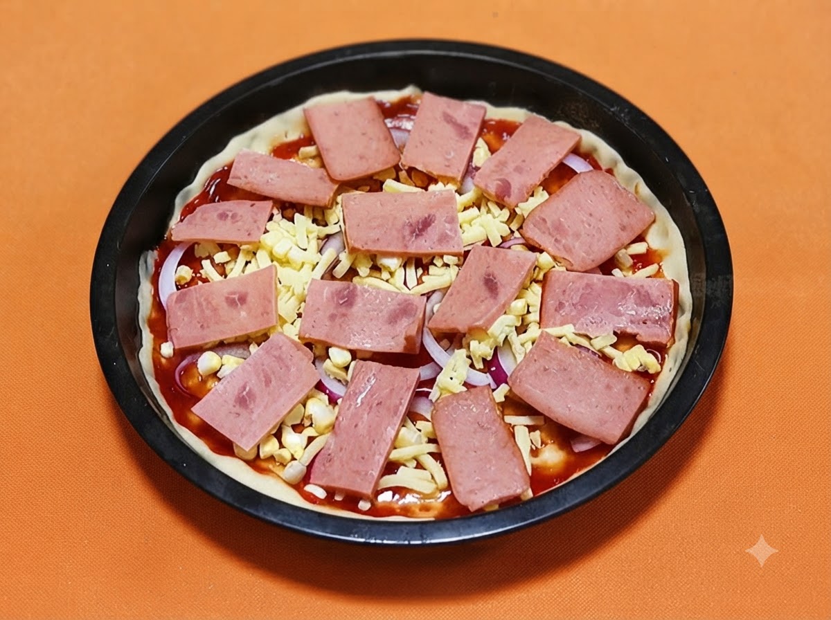 Prostokątnate plastry różowej szynki ułożone systematycznie na spodzie do pizzy posypanym serem i cebulą.