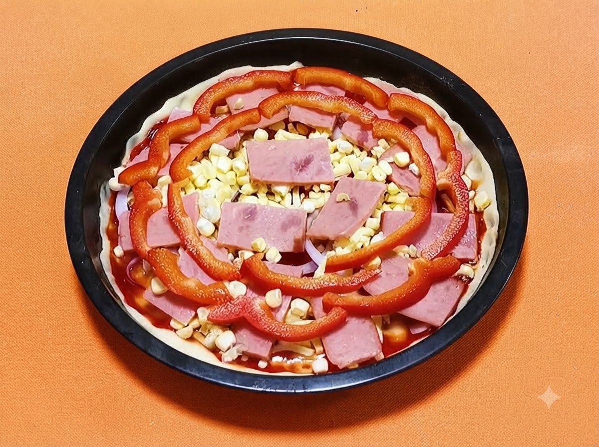 Spód pizzy w czarnej formie pokryty sosem, szynką, żółtymi ziarnami kukurydzy oraz plasterkami czerwonej papryki.