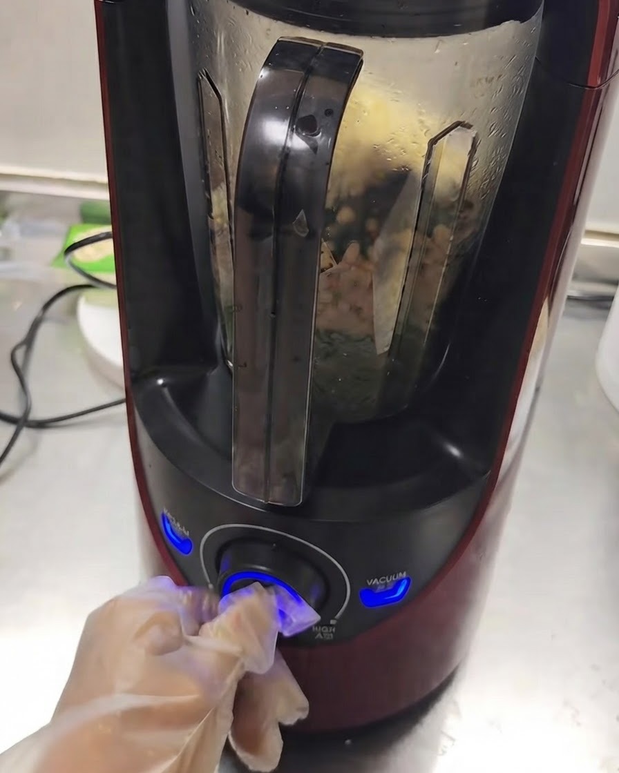 Działający blender z mieszającymi się wewnątrz składnikami, podczas gdy dłoń przekręca pokrętło.