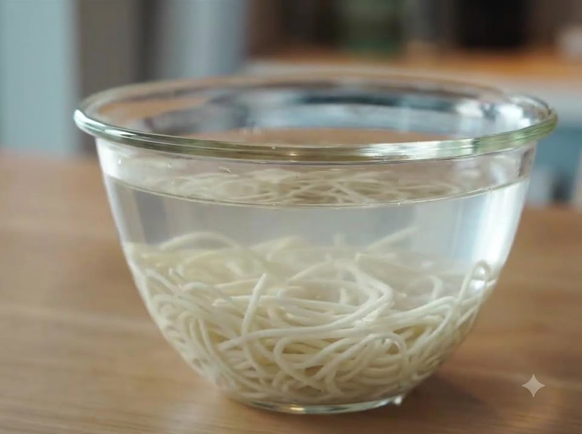 Świeżo ugotowany makaron ramen zanurzony w szklanej misce wypełnionej zimną wodą w celu schłodzenia.