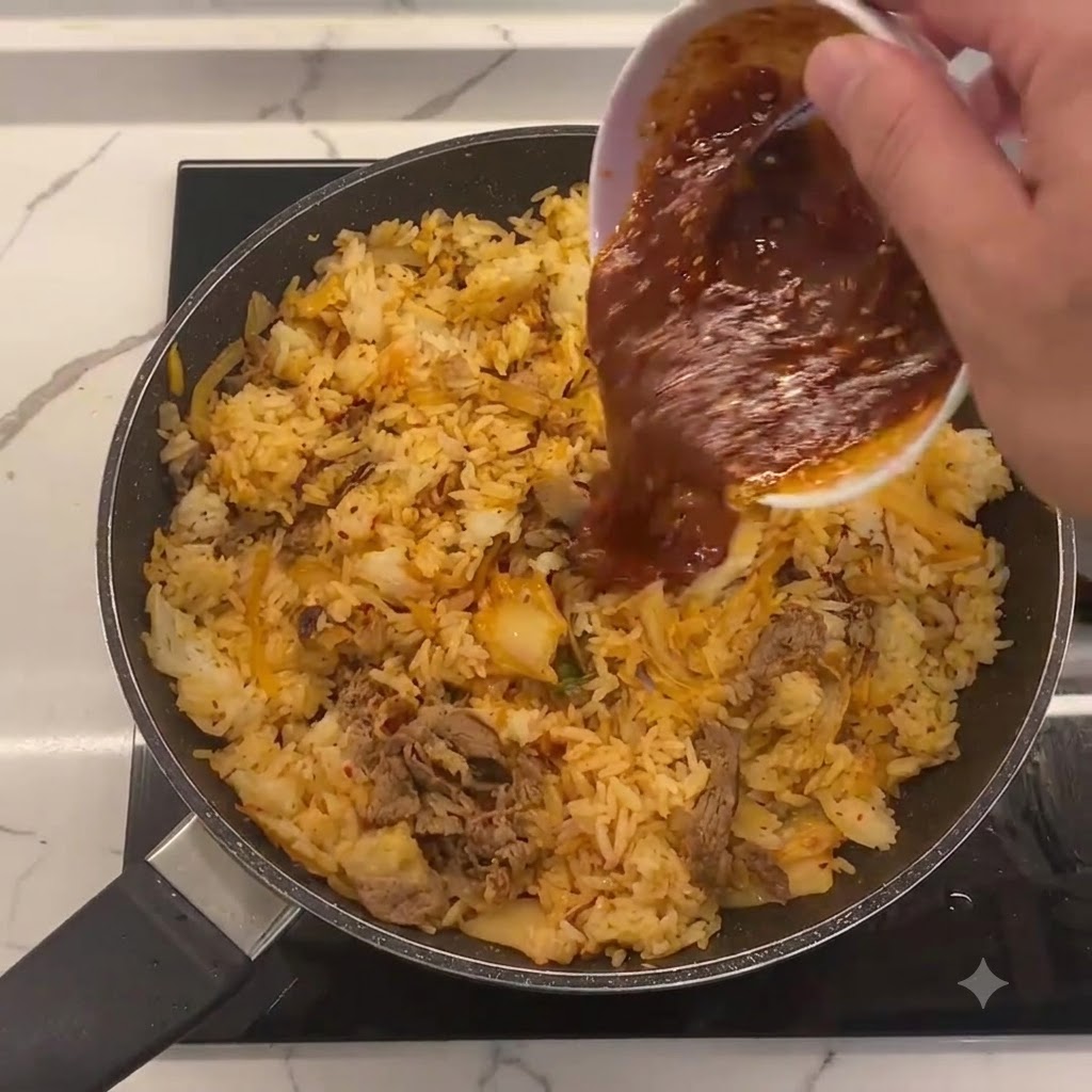 Specjalny sos wlewany z małej białej miseczki na środek patelni z ryżem, kimchi i wołowiną.