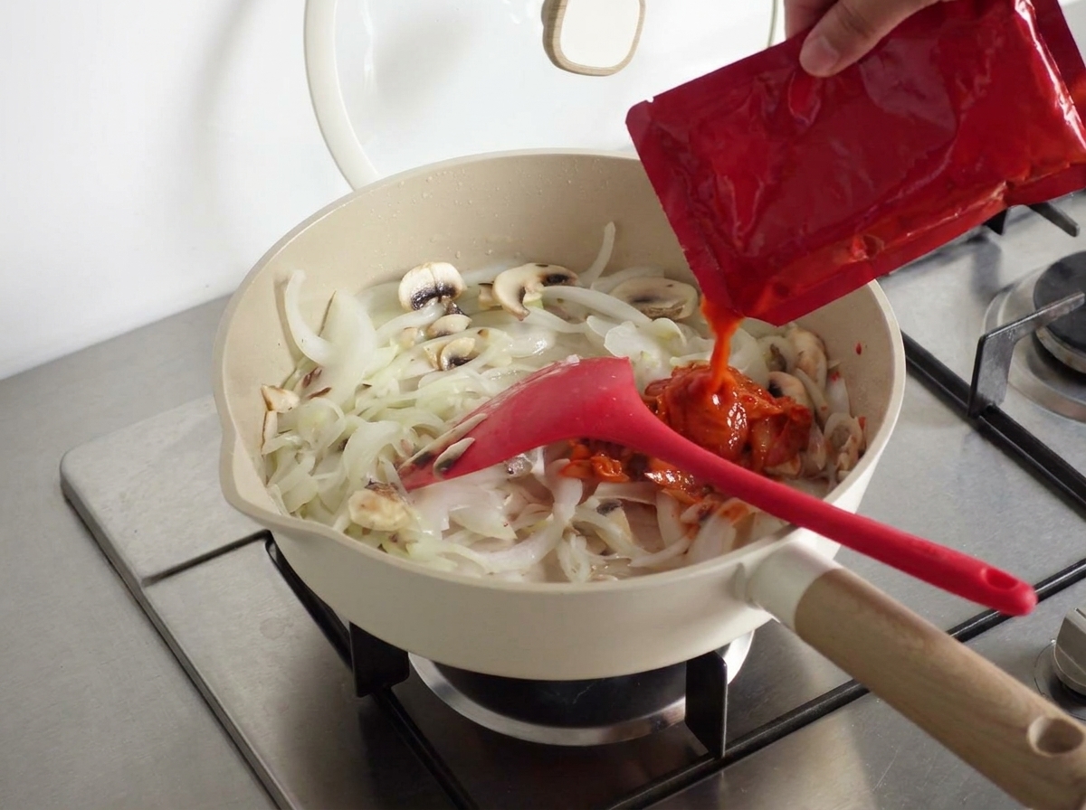 Łyżka koreańskiej pasty chili dodawana do składników na patelni.