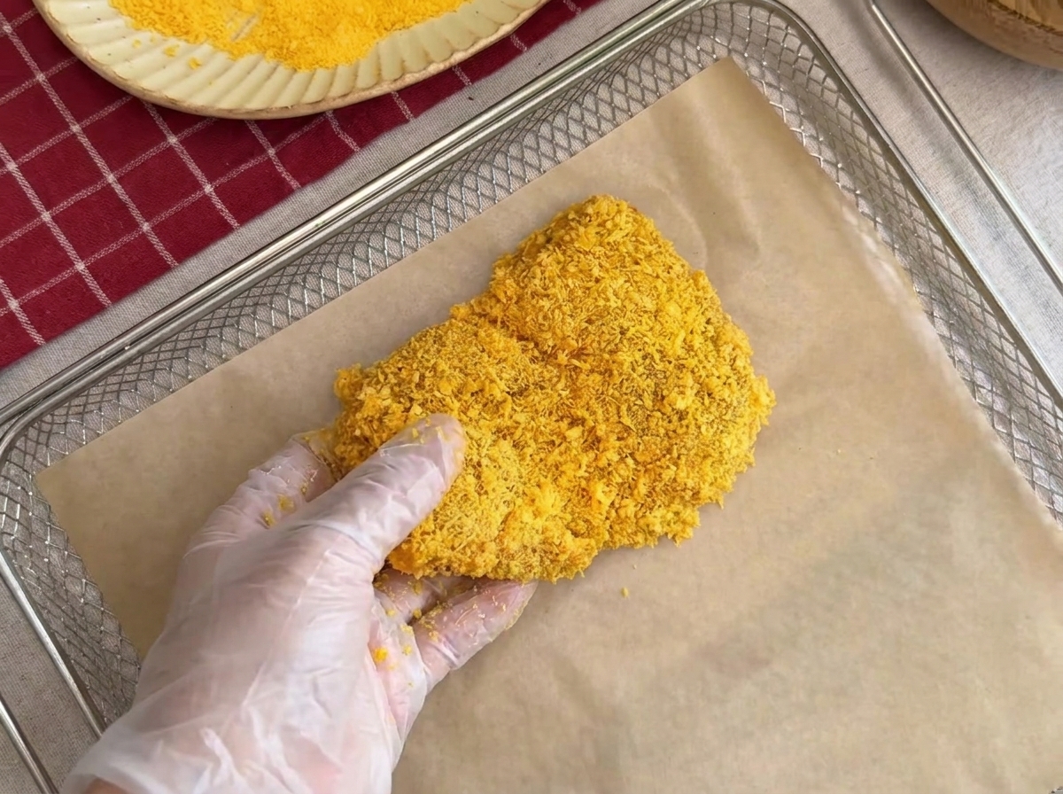 Opanierowany kotlet schabowy układany ostrożnie na ruszcie wyłożonym papierem do pieczenia.