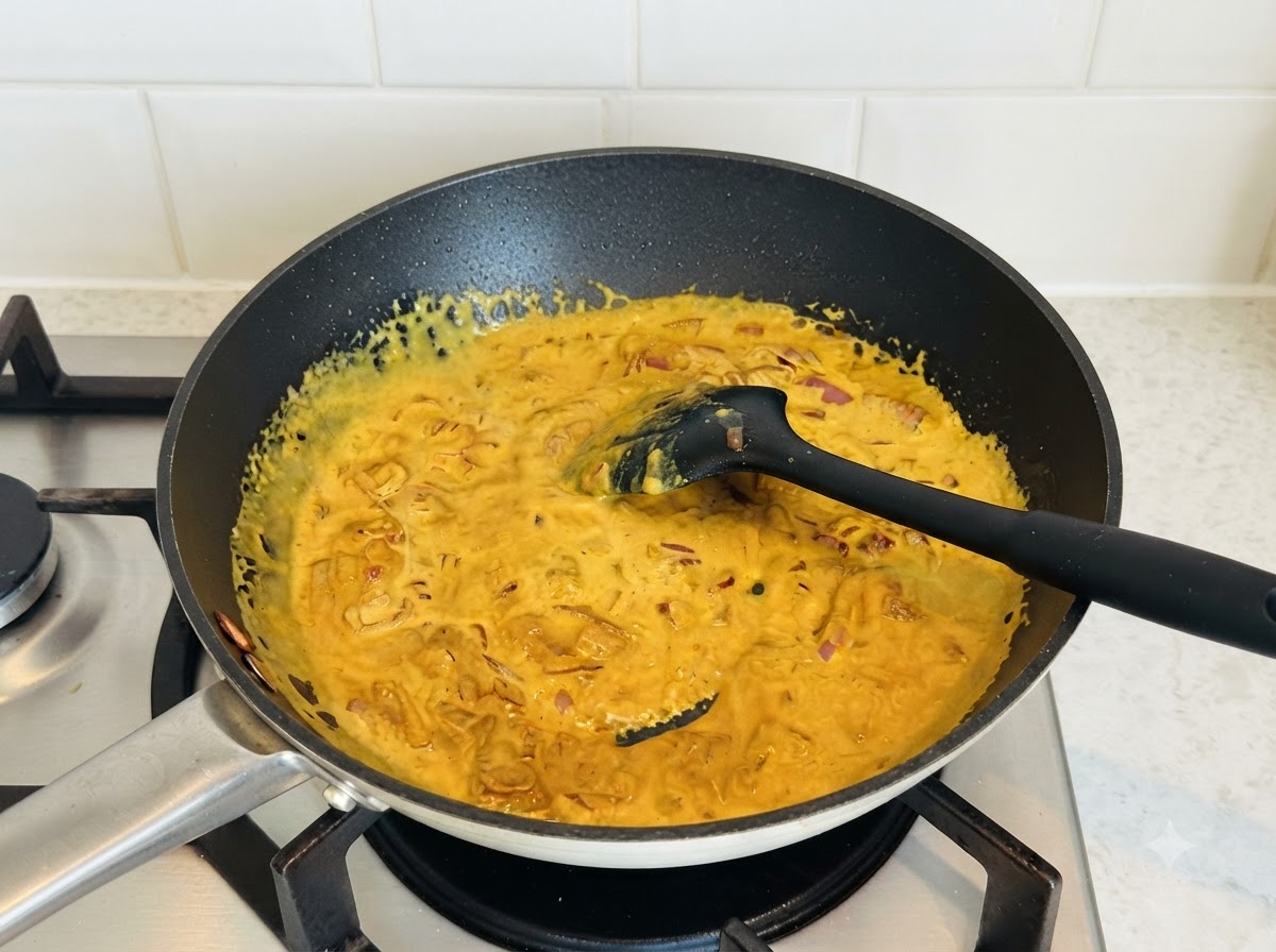 Gęsty, żółty sos curry mieszany na ciemnej patelni czarną silikonową łopatką.