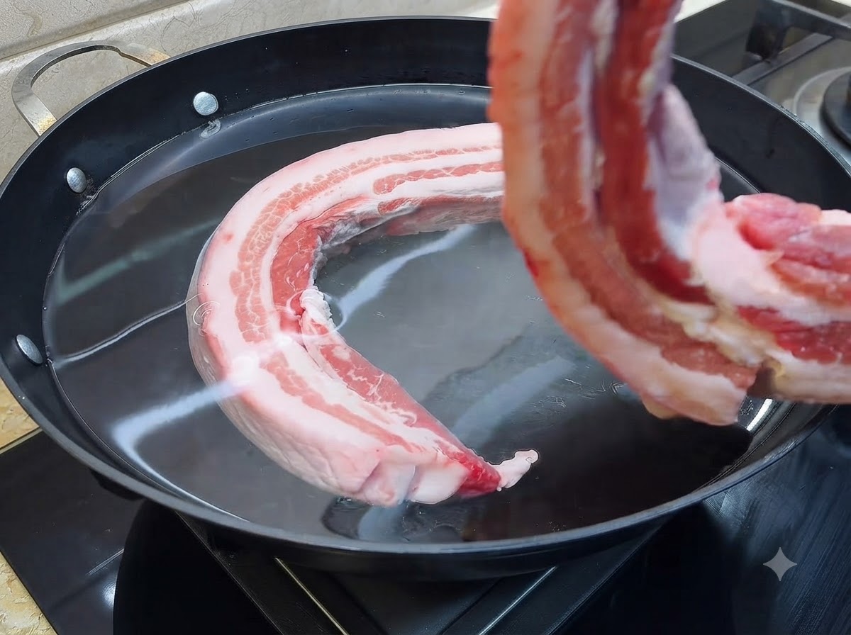 Kawałek surowego boczku wieprzowego wkładany do dużego garnka wypełnionego zimną wodą.