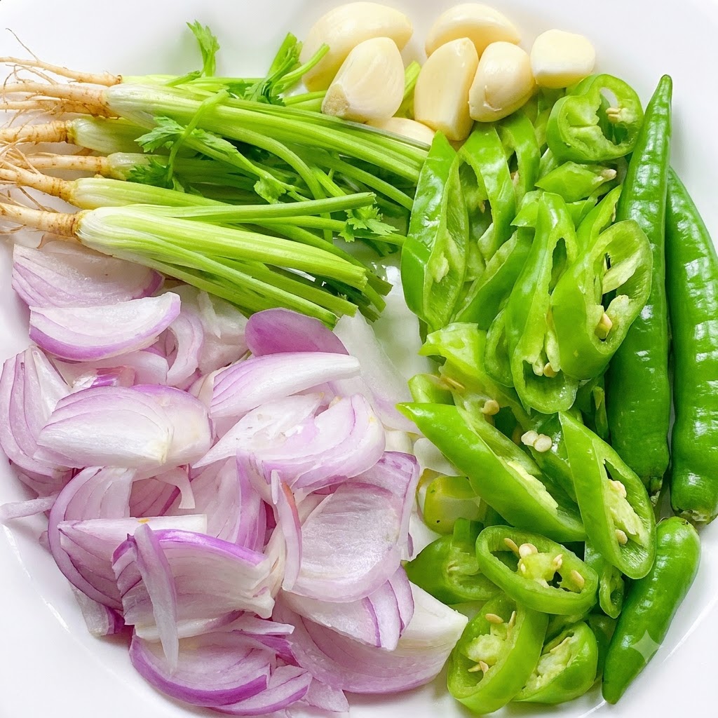 Świeże korzenie kolendry, pokrojone zielone chili, posiekaną szalotkę i całe ząbki czosnku ułożone na białym talerzu.