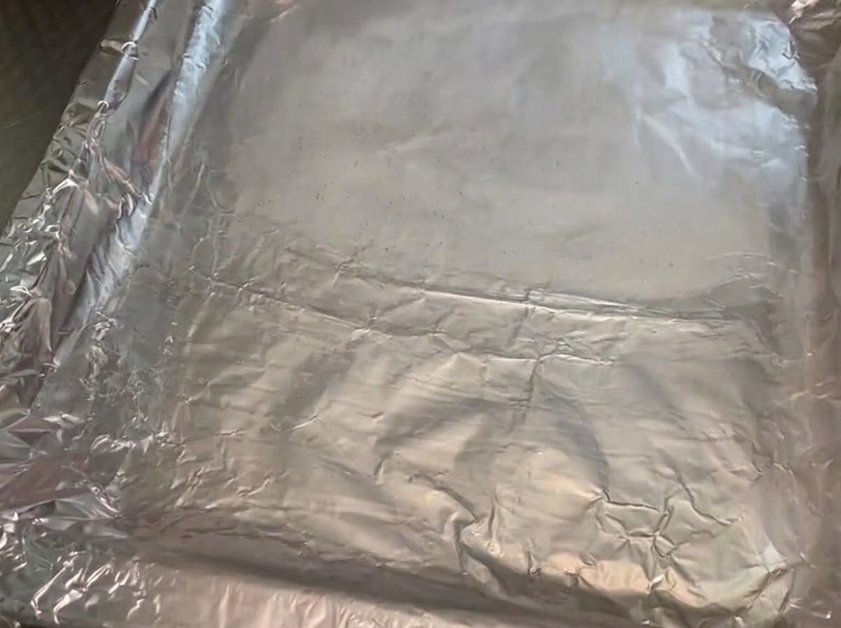 Metalowa blacha wyłożona pogniecioną folią aluminiową, posmarowana błyszczącą warstwą oleju roślinnego.