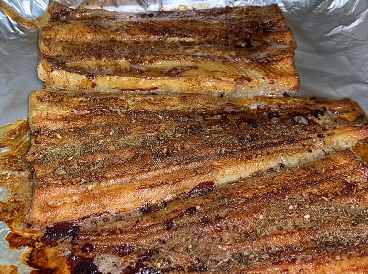 Upieczone filety z węgorza równomiernie oprószone warstwą brązowej przyprawy BBQ w formie do pieczenia.
