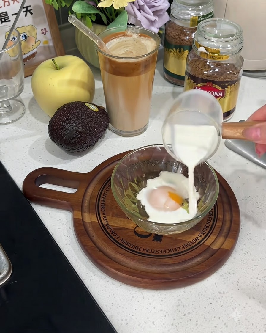 Mleko nalewane z małego szklanego dzbanka do miski zawierającej rozbite jajko.